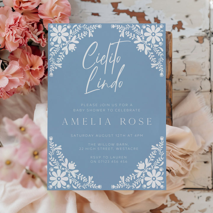 Boho Cielito Lindo baby shower card with folk-inspired white flowers and modern typography, set on a woven background.