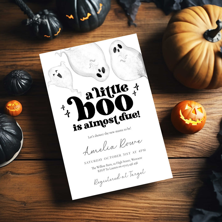 Halloween-themed baby shower invitation with ghosts and pumpkins on a wooden table.