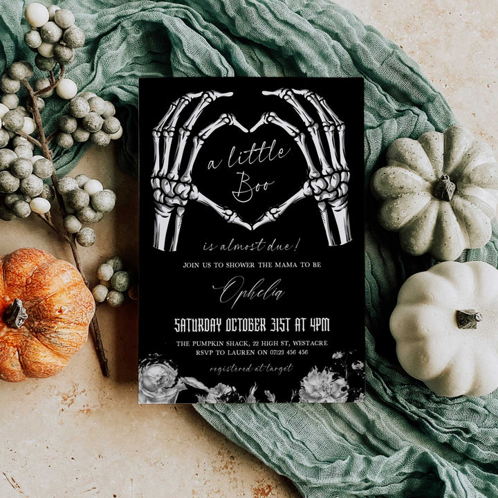 Black and white skeleton hand baby shower invite with gothic lettering and floral accents, perfect for October event.