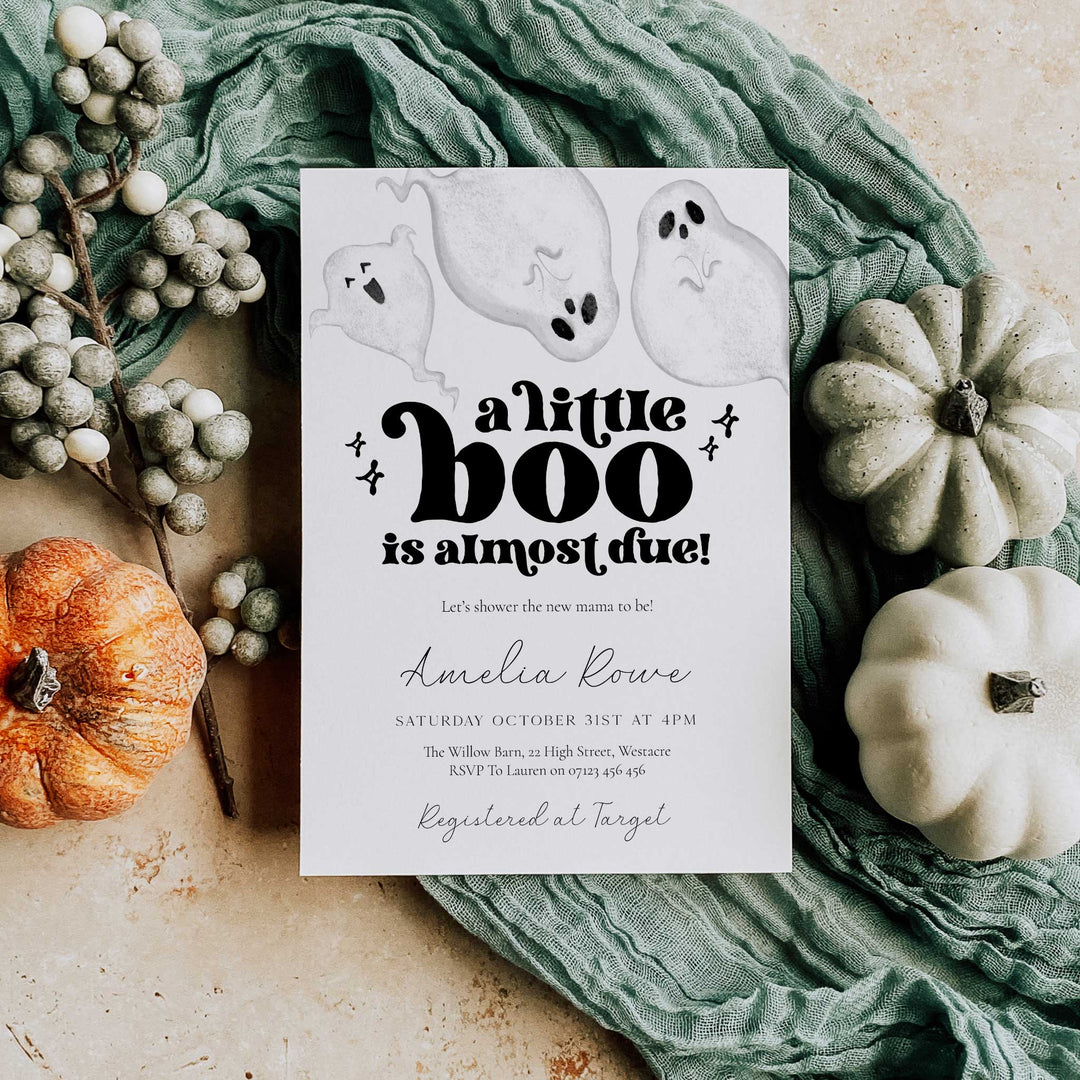 Halloween-themed baby shower invitation with pumpkins and ghost decorations on a textured surface.
