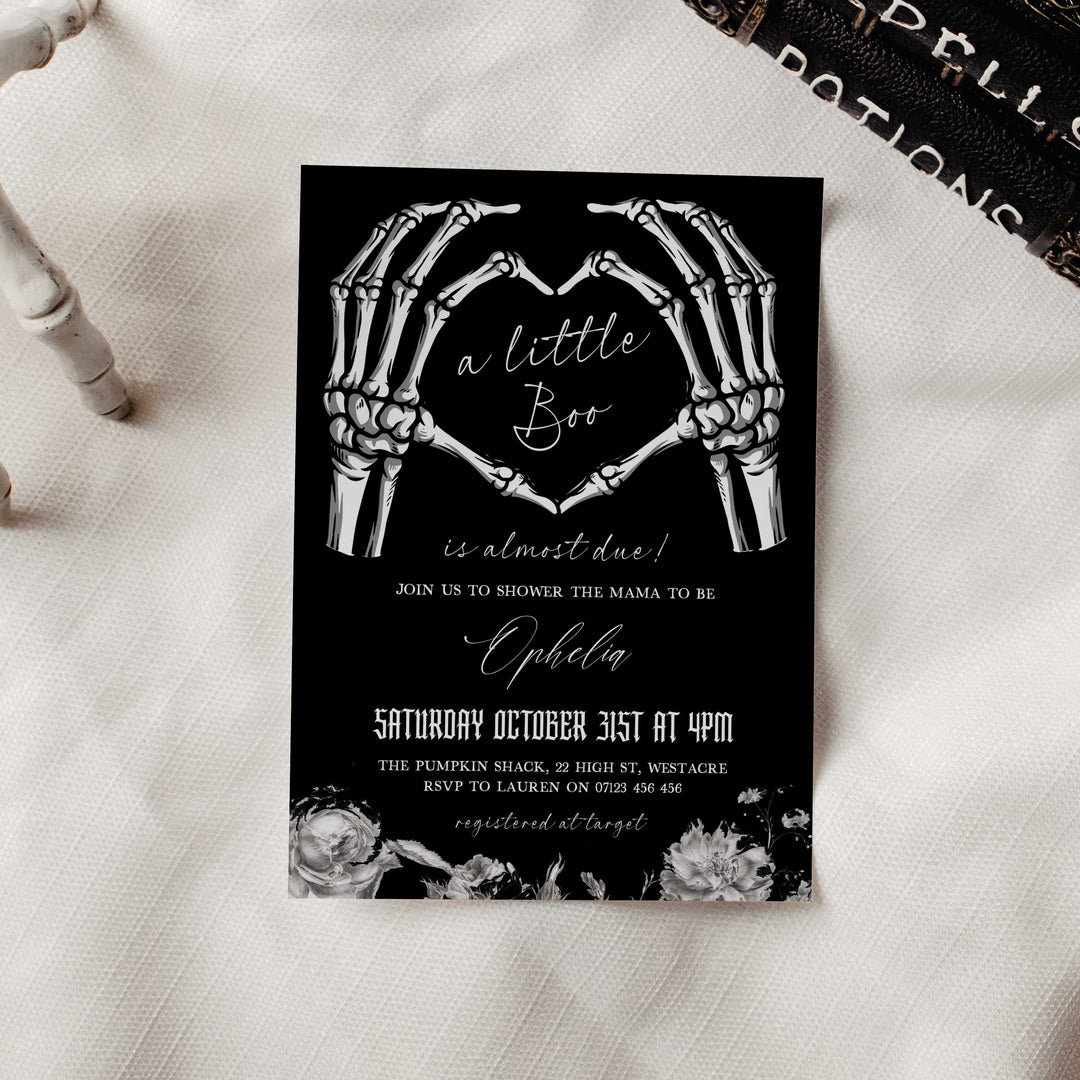 Black Halloween baby shower invitation with skeleton heart hands and elegant white florals for spooky yet classy theme.