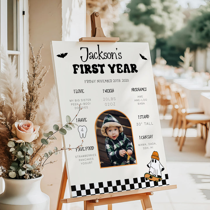 Ghost-themed first birthday board with skeleton hand design, baby’s photo, and fun nicknames, ideal for October celebrations.