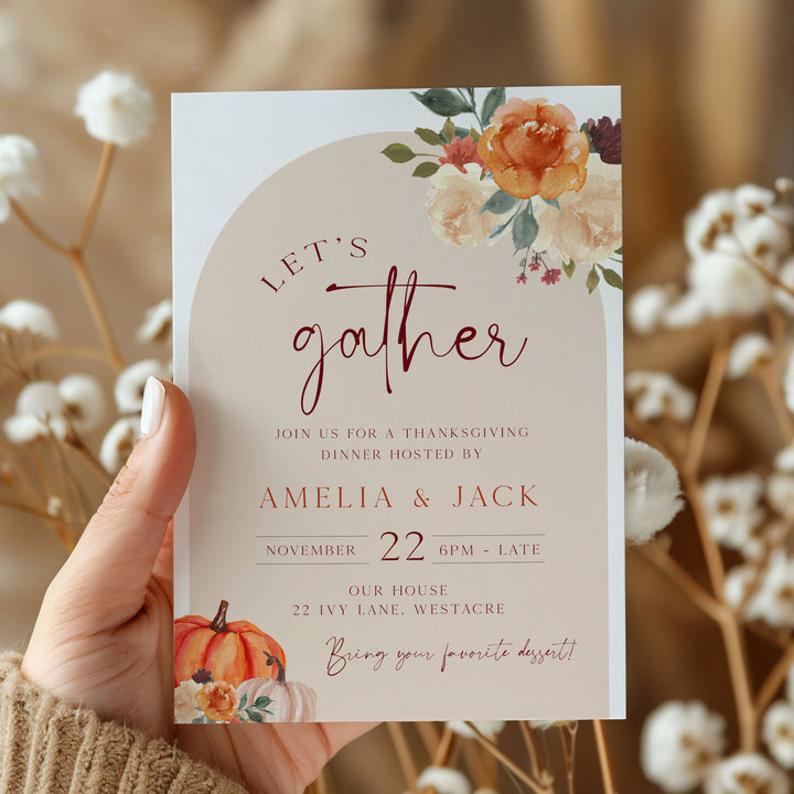 Custom holiday dinner invitation with hand lettering and floral pumpkins, held in a cozy sweatered hand.